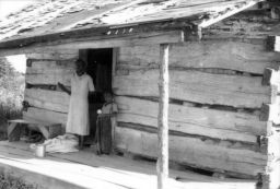 Black woman and child standing on the porch of a wooden shack