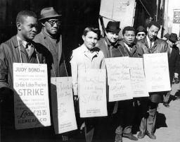 White and African American male strikers of ILGWU Local 23-25 wear signs while picketing against Judy Bond blouses.