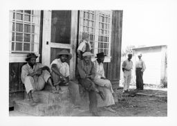 A group of Black men relaxing in the shade at a gas station in Delta Cooperative