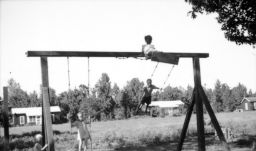 Children playing on a swings at Delta Cooperative with houses in the background