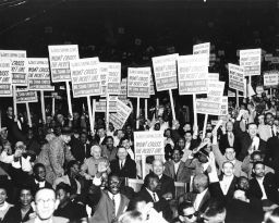 White and African American males hold signs that read: "The Dress Shipping Clerks' Won't Cross the Picket Line.  We Stand United with the Dressmakers Union!" 1958.