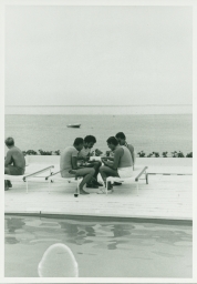 Men eating by poolside, overlooking the ocean, on Fire Island trip