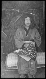 Ainu girl embroidering cloth outside chisei, undated