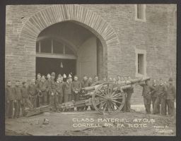 Student military posing with 4.7 inch gun by entrance of Barton Hall