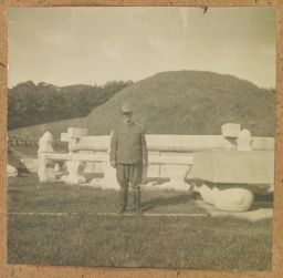 [Western man in uniform posing in front of burial mound]