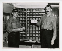 Two workers holding Shenandoah Central Railroad first anniversary envelopes by mail sorter in depot
