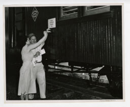 Man and woman place mail inside slot on the side of a train car signed Railway Express Agency