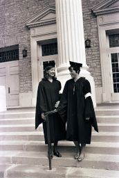 Two women students stand on steps of Main Hall on Commencement day