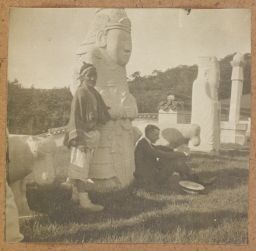 [Western man and Korean laborer resting by statues]