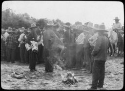 A large group of men in wide-brimmed hats, huddled together near a fire