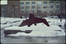 Metal sculpture outside the library, with Bard hall in the background and the ground is snow covered.