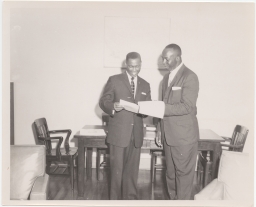 Jerome H. Holland and another man examining a document