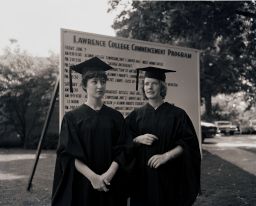 Two women students stand in caps and gowns