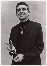 Daniel Berrigan in handcuffs making a peace sign and wearing pendant
