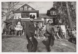 Policeman standing in front of a crowd outside a house.