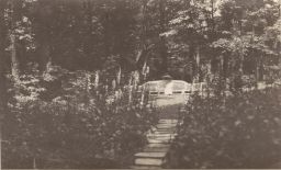 Woman with parasol on bench in rear, path and trees in foreground