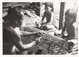 Man making fish trap; 2 children watching