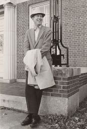 Archie Ammons leaning against building, holding coat, smiling