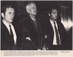 Philip Berrigan being escorted in handcuffs by two men in suits