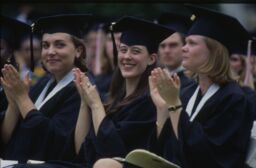 Three graduates clap during Commencement