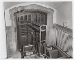 Arched double doors, tied with wire, with chairs and a coat rack piled against them in Willard Straight Hall.