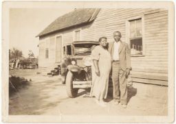 Man and woman standing in front of a car and a house
