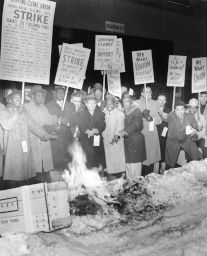 Striking African American and white shipping clerks try to keep warm as they picket for better wages and union recognition.