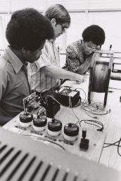 Three men at electical engineering lab bench