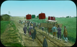 A line of Japanese individuals, some with banners, process down a dirt road in a lush field