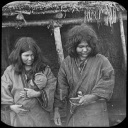 Two Ainu women, one carrying an infant, outside chise
