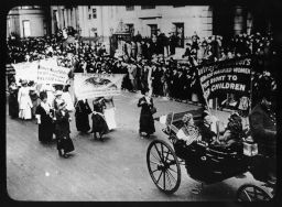 Women in horse-drawn carriage and on foot  march in street for voting rights carrying banners "Mothers Prepare the Children for the World..." "Women Need Votes..." and "Suffrage Pioneers..."