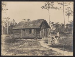 Two slave children stand in front of a log cabin, while another peeks out from the window