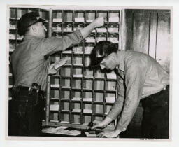 Two workers sorting and stamping mail inside depot