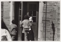 Man carrying a baby walking in a back door of Willard Straight.