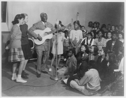 Photo of Lead Belly (Huddie William Ledbetter, Leadbelly) playing for a female audience
