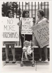 Three women with a baby in a stroller holding protest signs