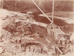 Construction of dam at Cornell Hydraulic Laboratory: stone dam wall, with Beebe Lake in background.
